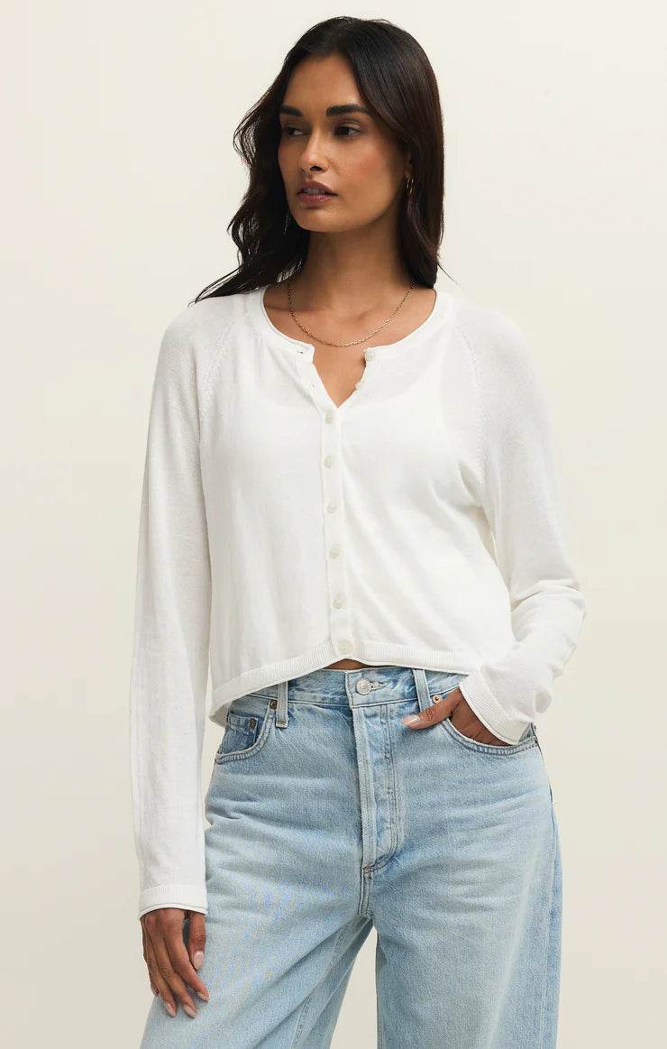Woman wearing a white cardigan and light blue jeans against a plain background