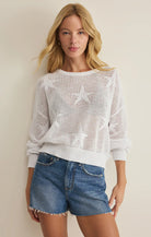 Woman wearing a white star-patterned sweater and denim shorts against a plain background