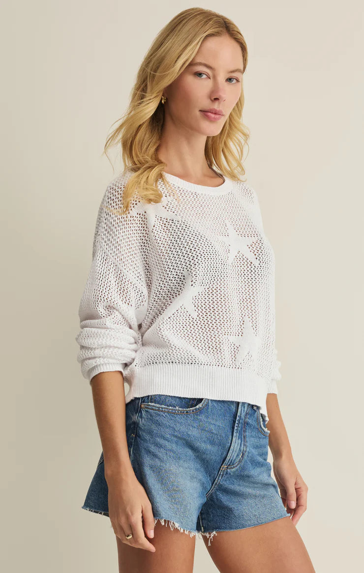 Woman wearing a white knit sweater and denim shorts on a beige background