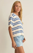 Woman wearing a blue and white striped sweater with denim shorts on a beige background