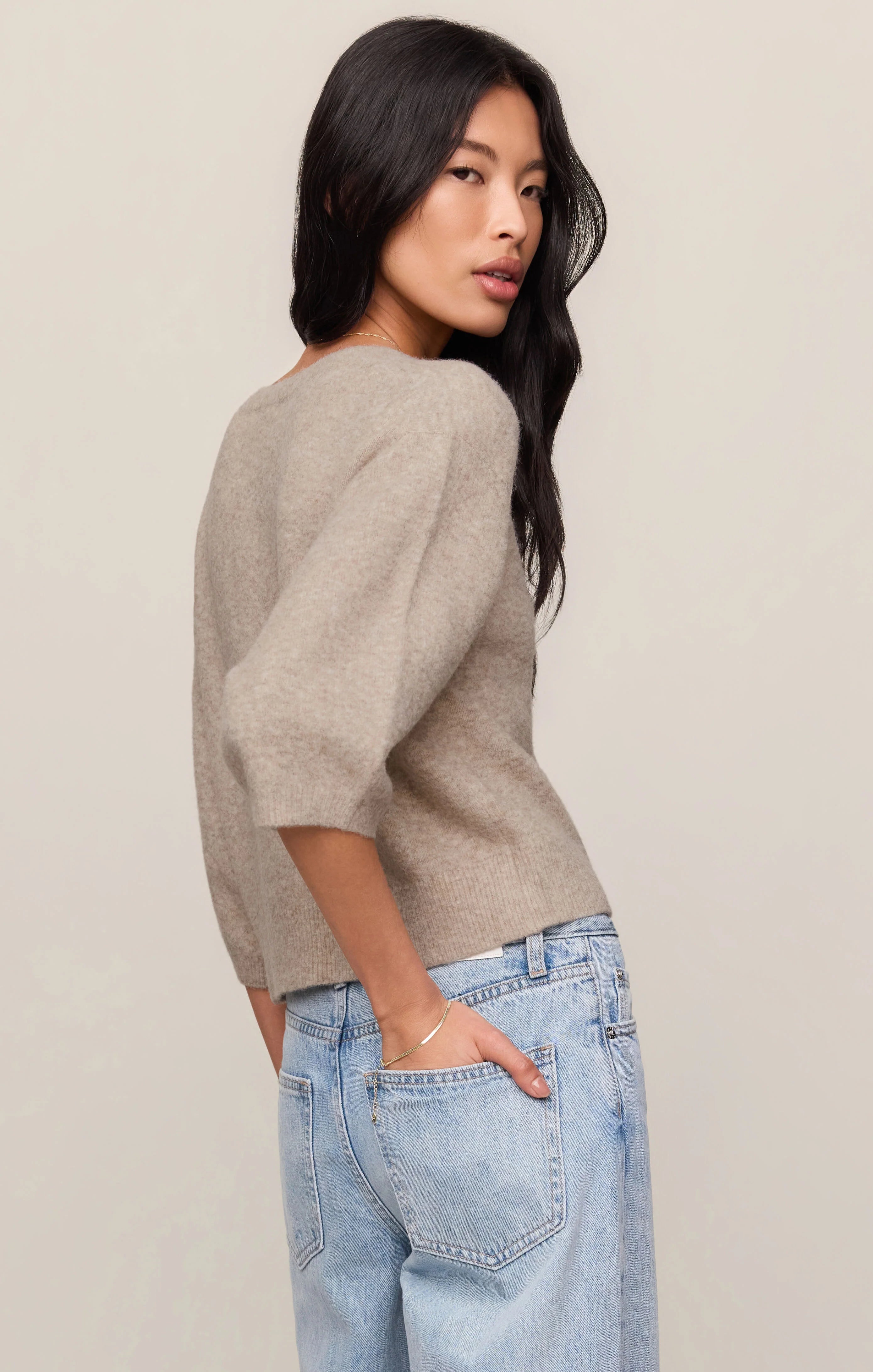 Woman wearing a beige sweater and light blue jeans against a plain background