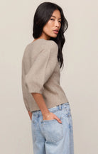 Woman wearing a beige sweater and light blue jeans against a plain background