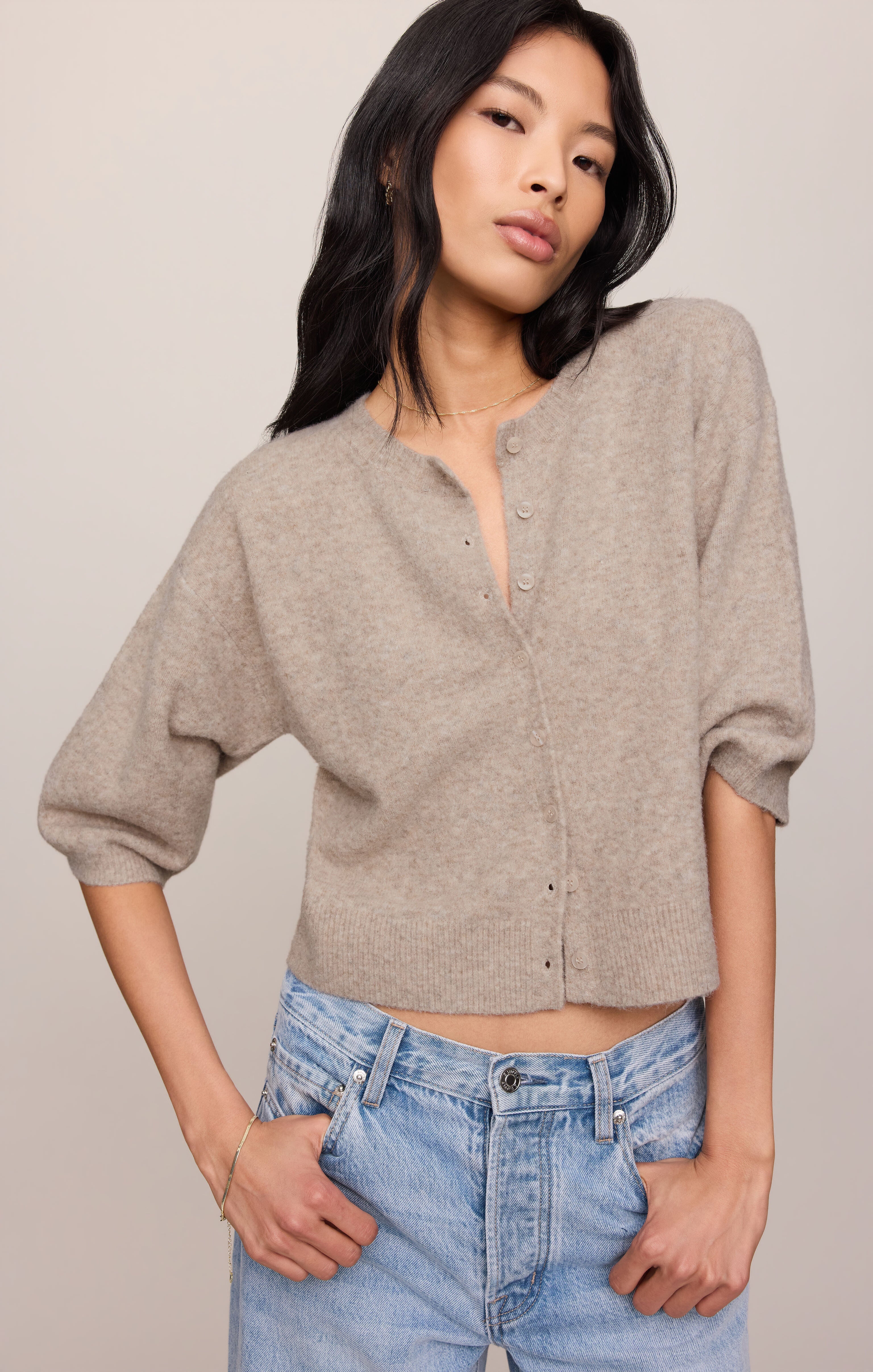 Woman wearing a beige button-up shirt and blue jeans against a plain background