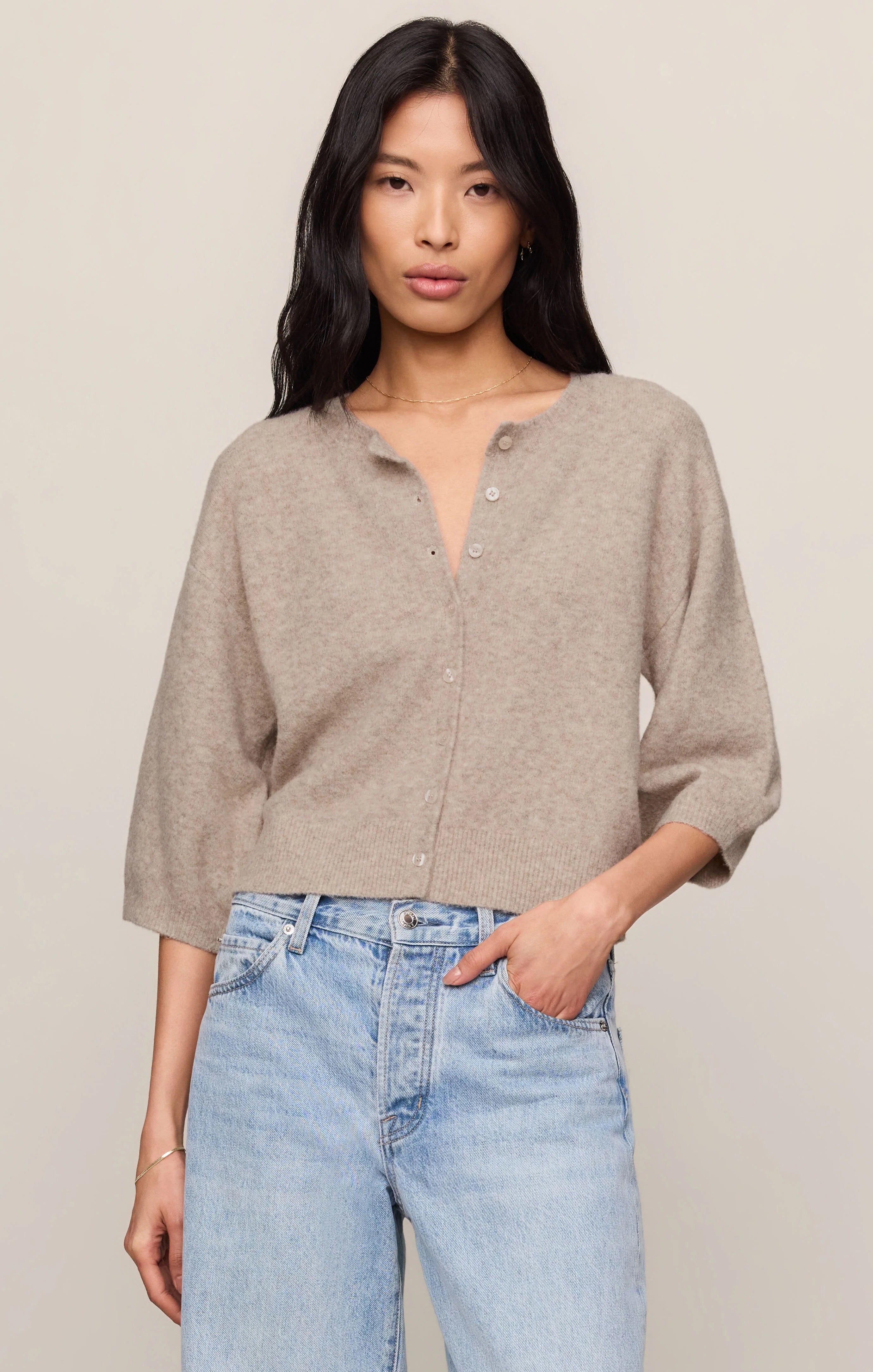 Woman wearing a beige cardigan and light blue jeans against a plain background