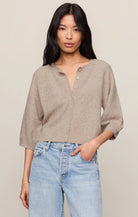 Woman wearing a beige cardigan and light blue jeans against a plain background