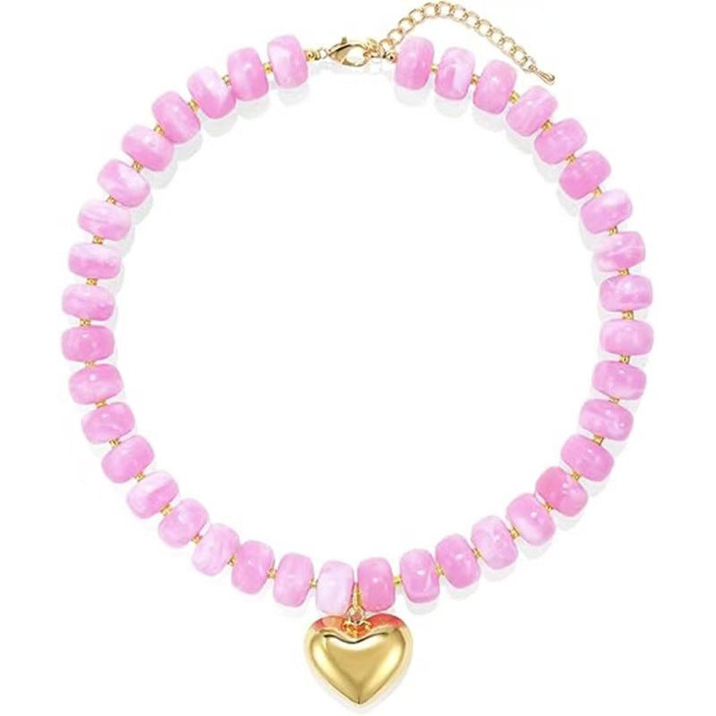 A pink beaded necklace with a gold heart pendant and gold chain clasp, displayed on a clean white background.