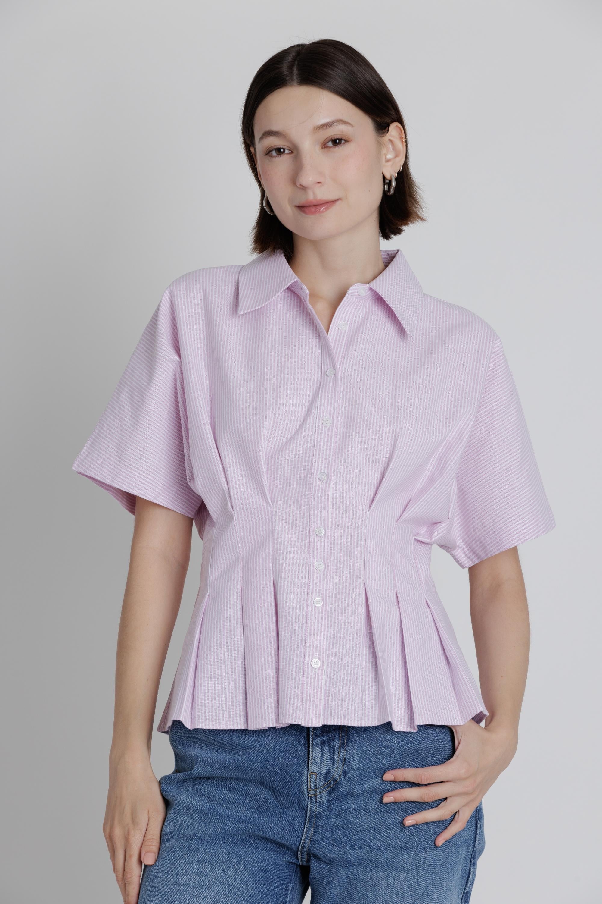 Woman wearing a light purple/pink button-up shirt and blue jeans against a plain background