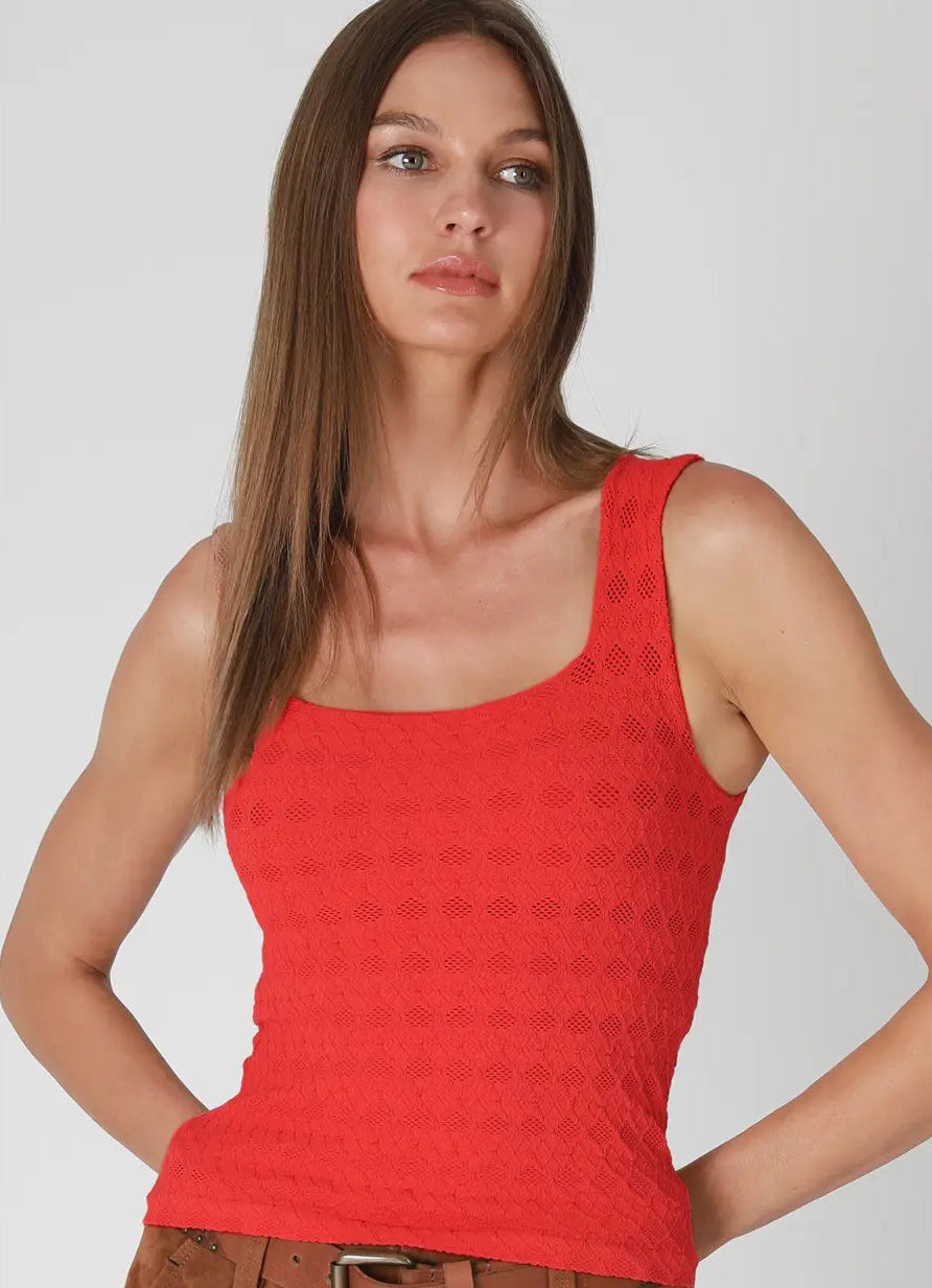 A woman modeling a textured red scoop-neck tank top, paired with brown pants and a brown belt, against a light gray background. 