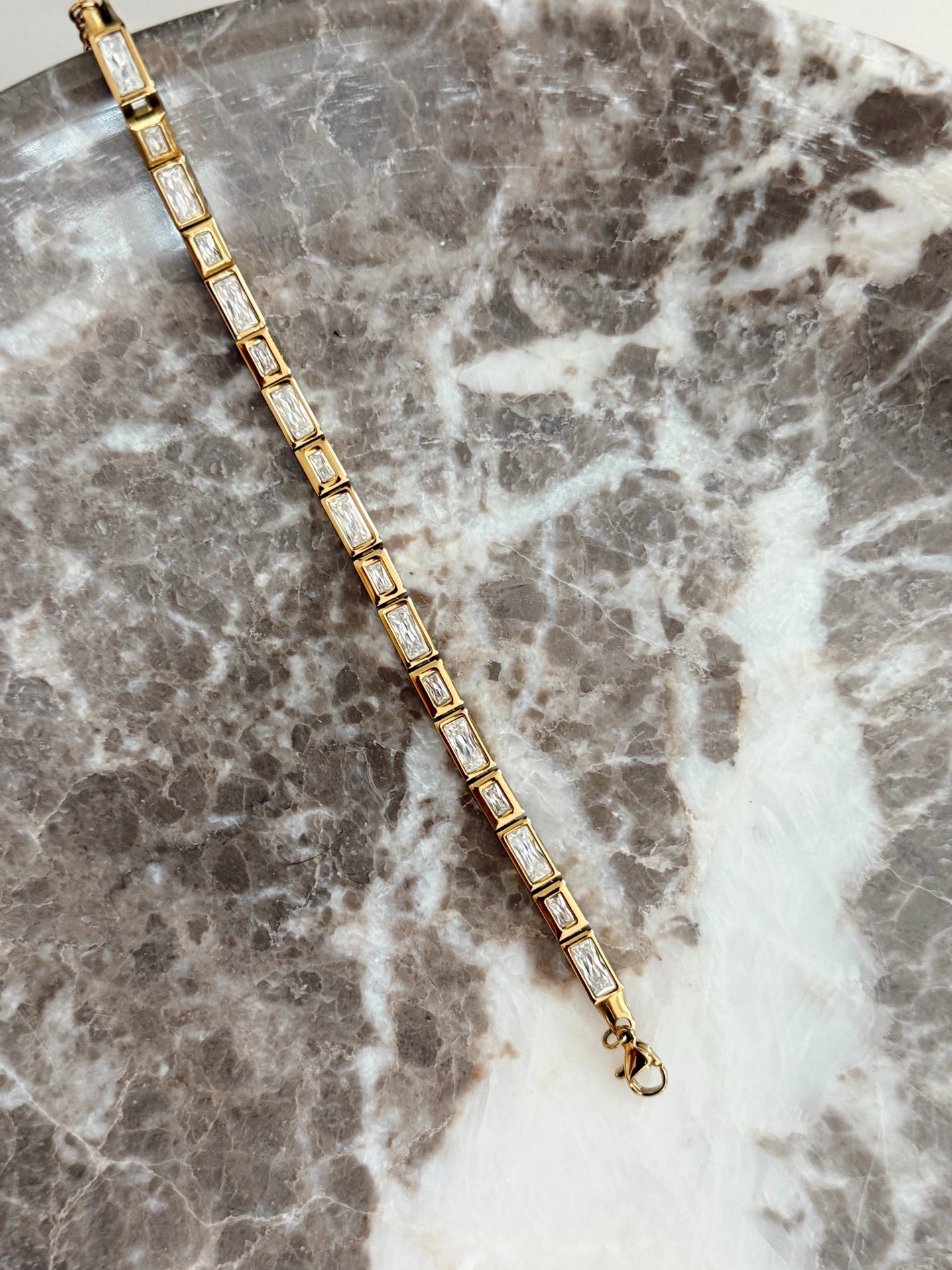 Gold bracelet with clear stones on a marble surface