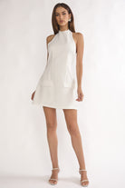 Woman wearing a white halter neck dress on a plain background