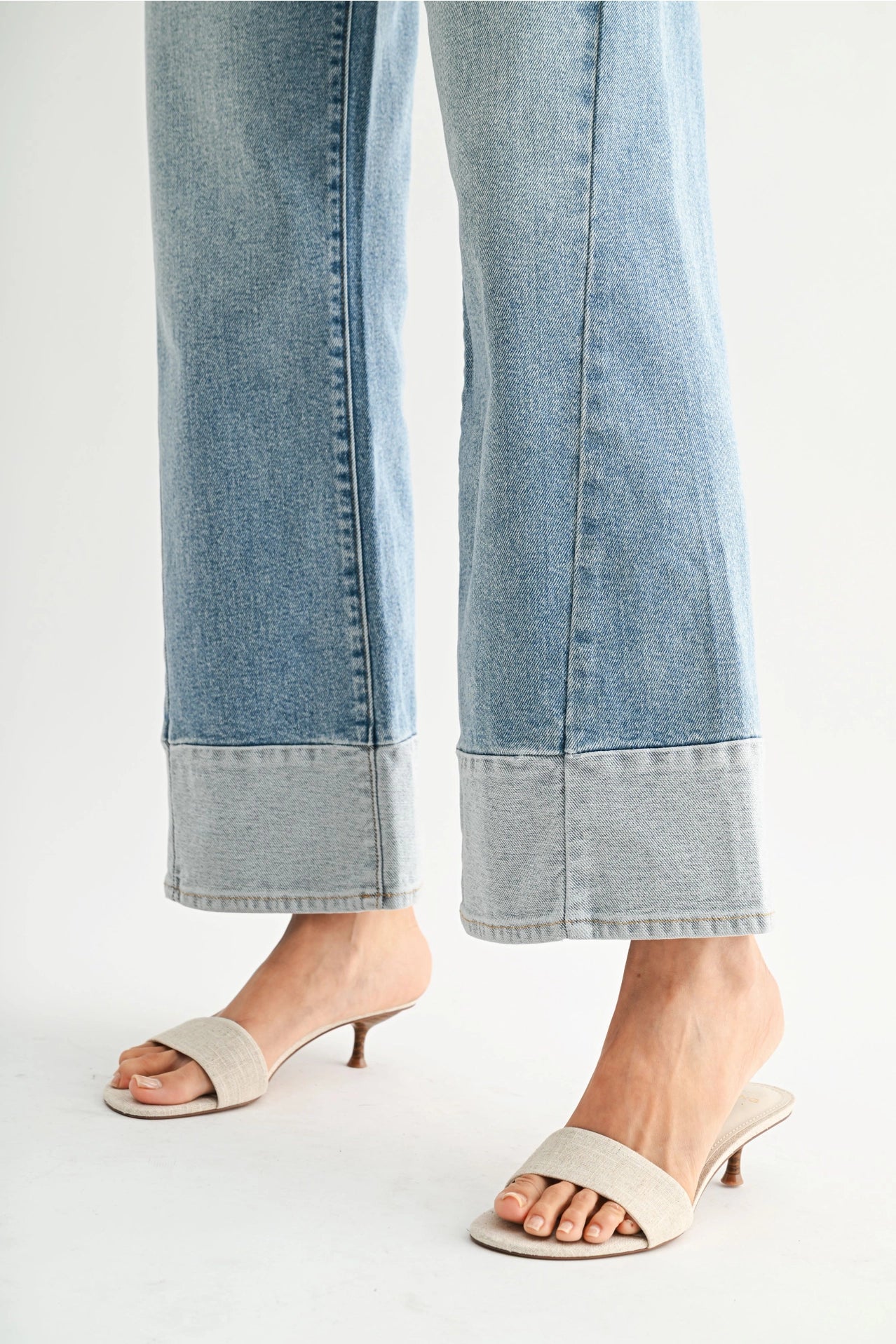 Light blue jeans with a cuffed hem worn by a person on a white background