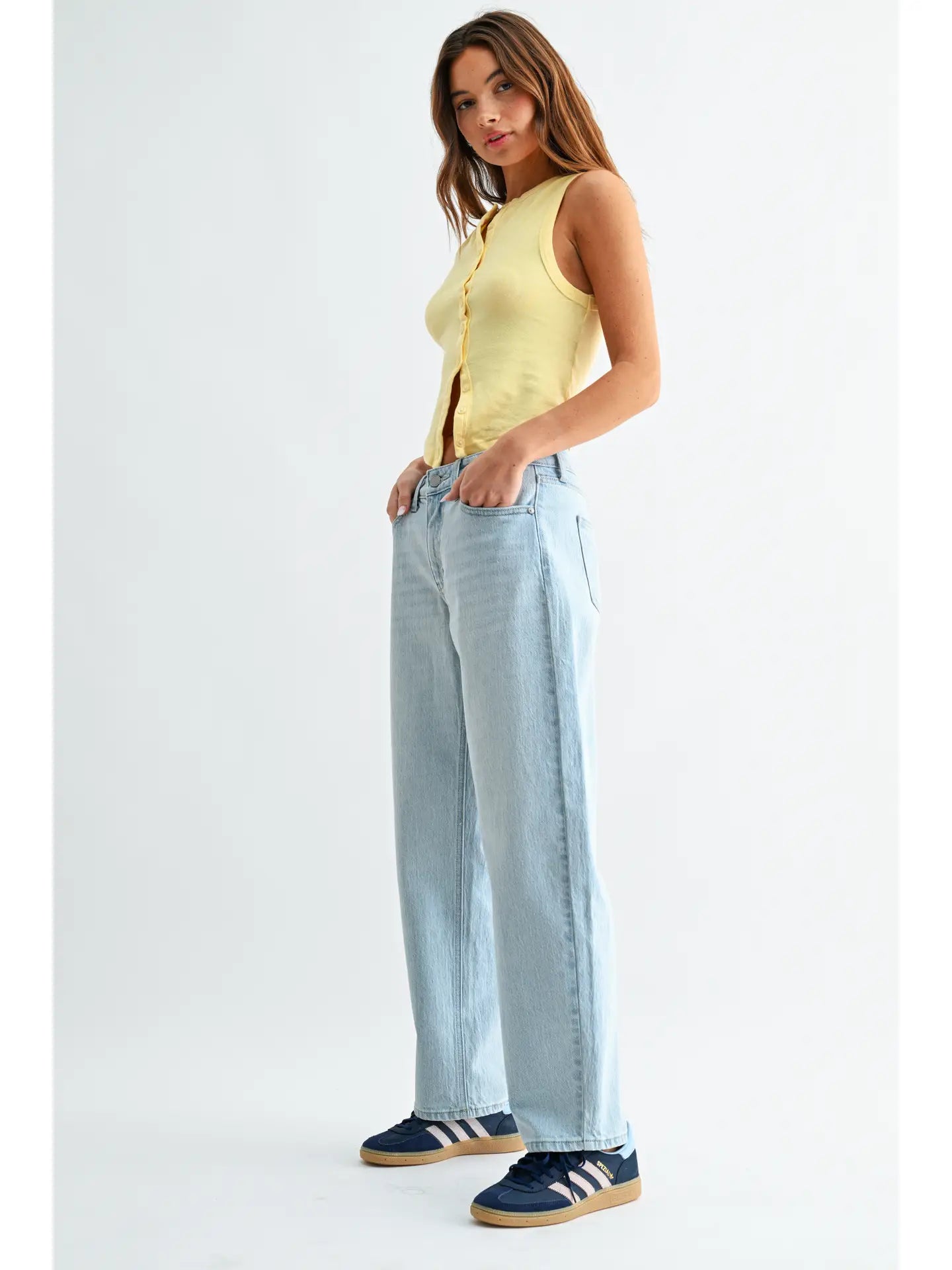 Woman wearing a yellow sleeveless top and light blue jeans on a white background