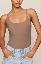Person wearing a brown bodysuit and light blue jeans against a neutral background