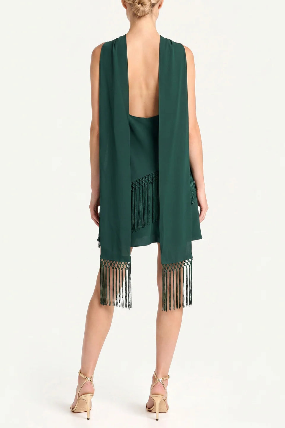 A model shown from the back wearing a dark green sleeveless open-front dress with fringe trim at the hem, paired with nude high-heeled sandals against a plain white studio background.