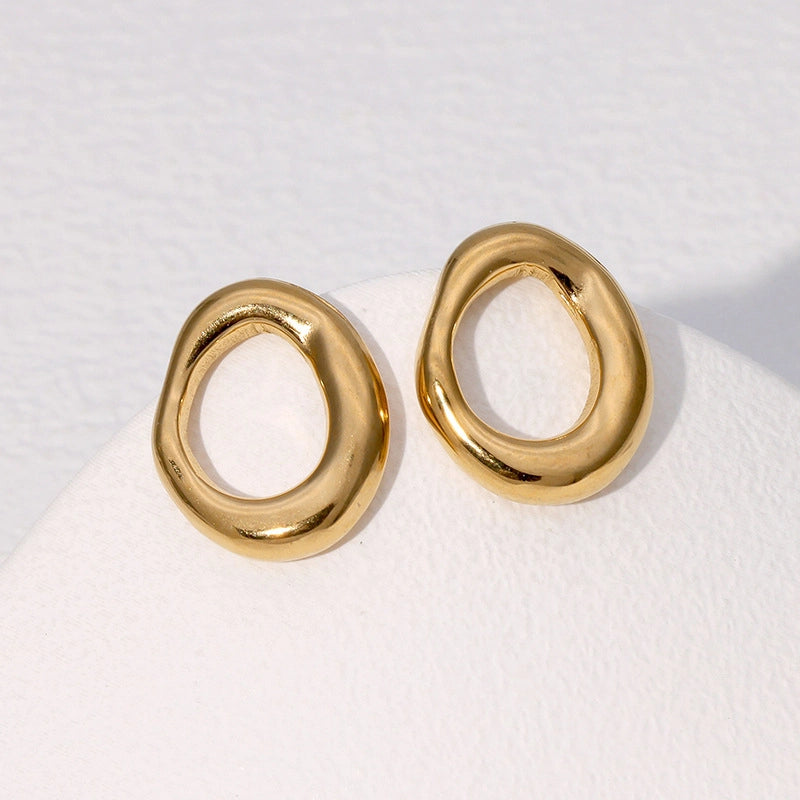 A pair of gold-toned, organic-shaped hoop earrings displayed on a white textured surface.
