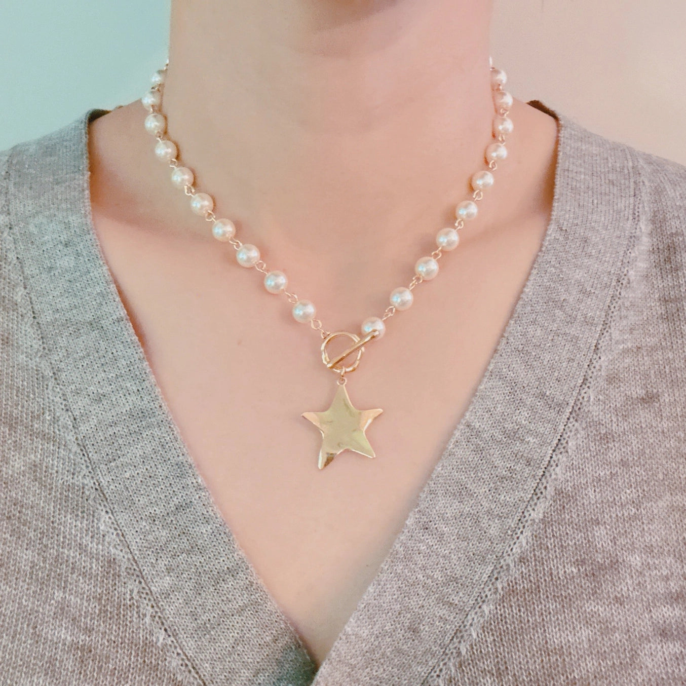 Pearl necklace with a gold star pendant worn by a person in a gray sweater.