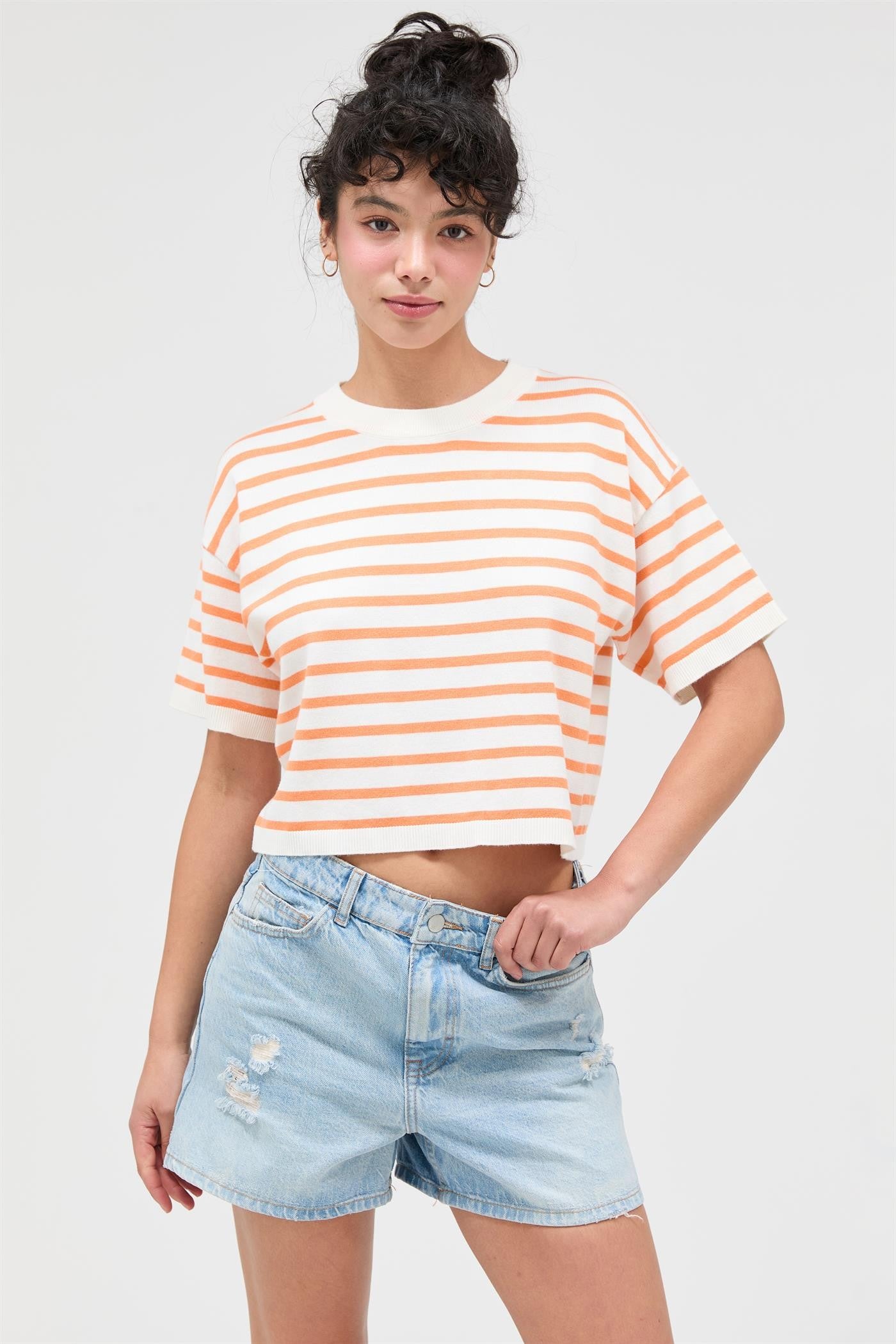 Person wearing a striped crop top and denim shorts on a plain background