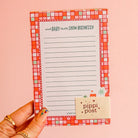 Notepad with a checkered border held by a hand on a pink background, featuring the brand 'pippi post'.