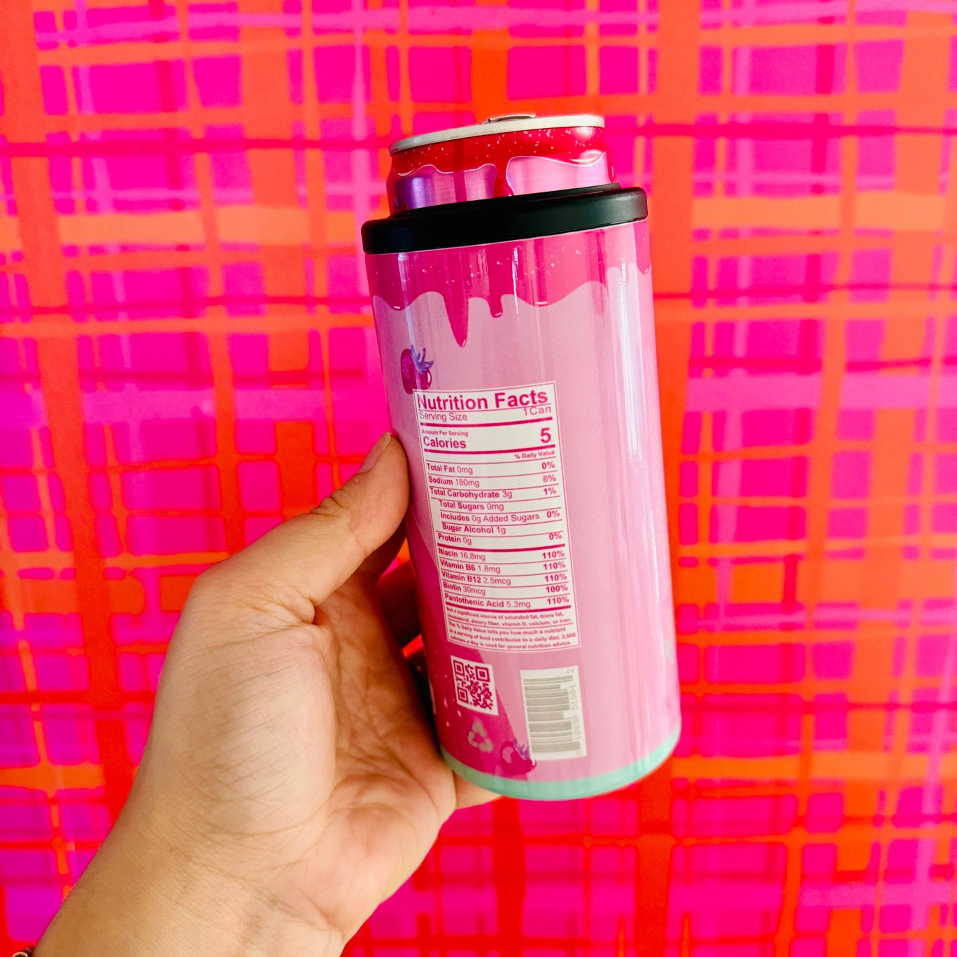 Hand holding a pink supplement container with a colorful plaid background