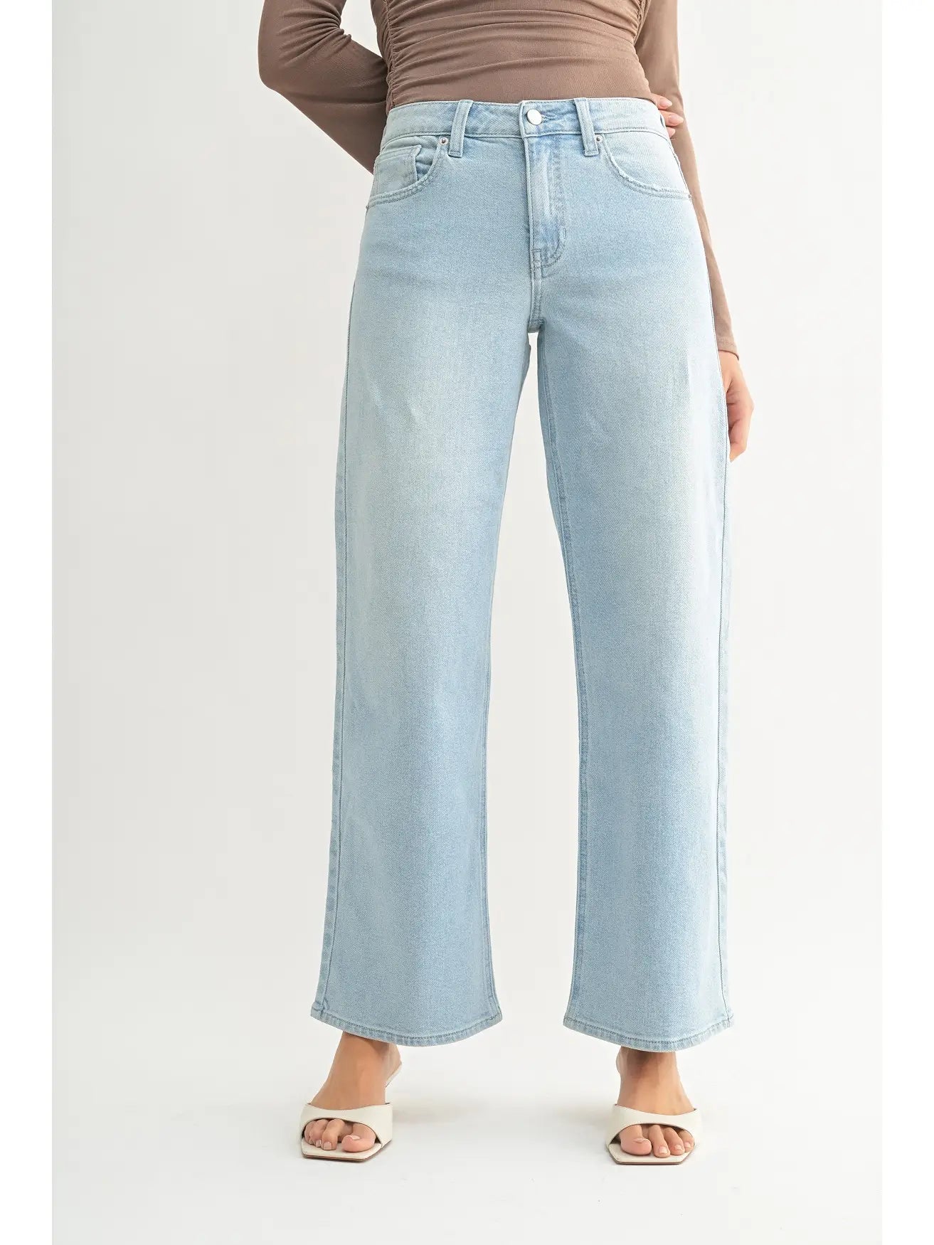 A model wearing light-wash wide-leg cropped jeans, a brown ribbed long-sleeve top, and white slide sandals, shown from the waist down against a plain off-white studio background.