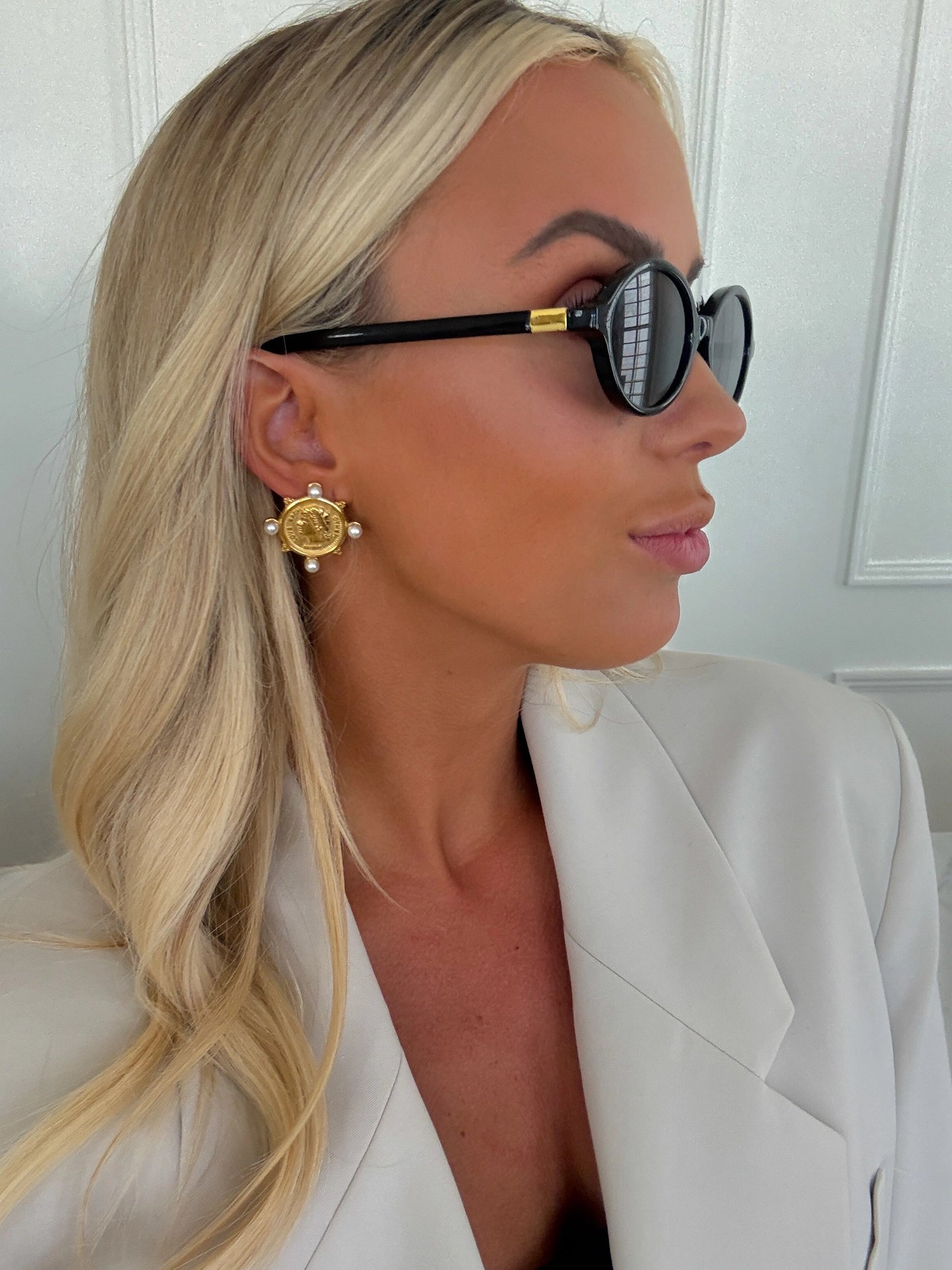 Woman wearing black sunglasses and a gold earring with a white background