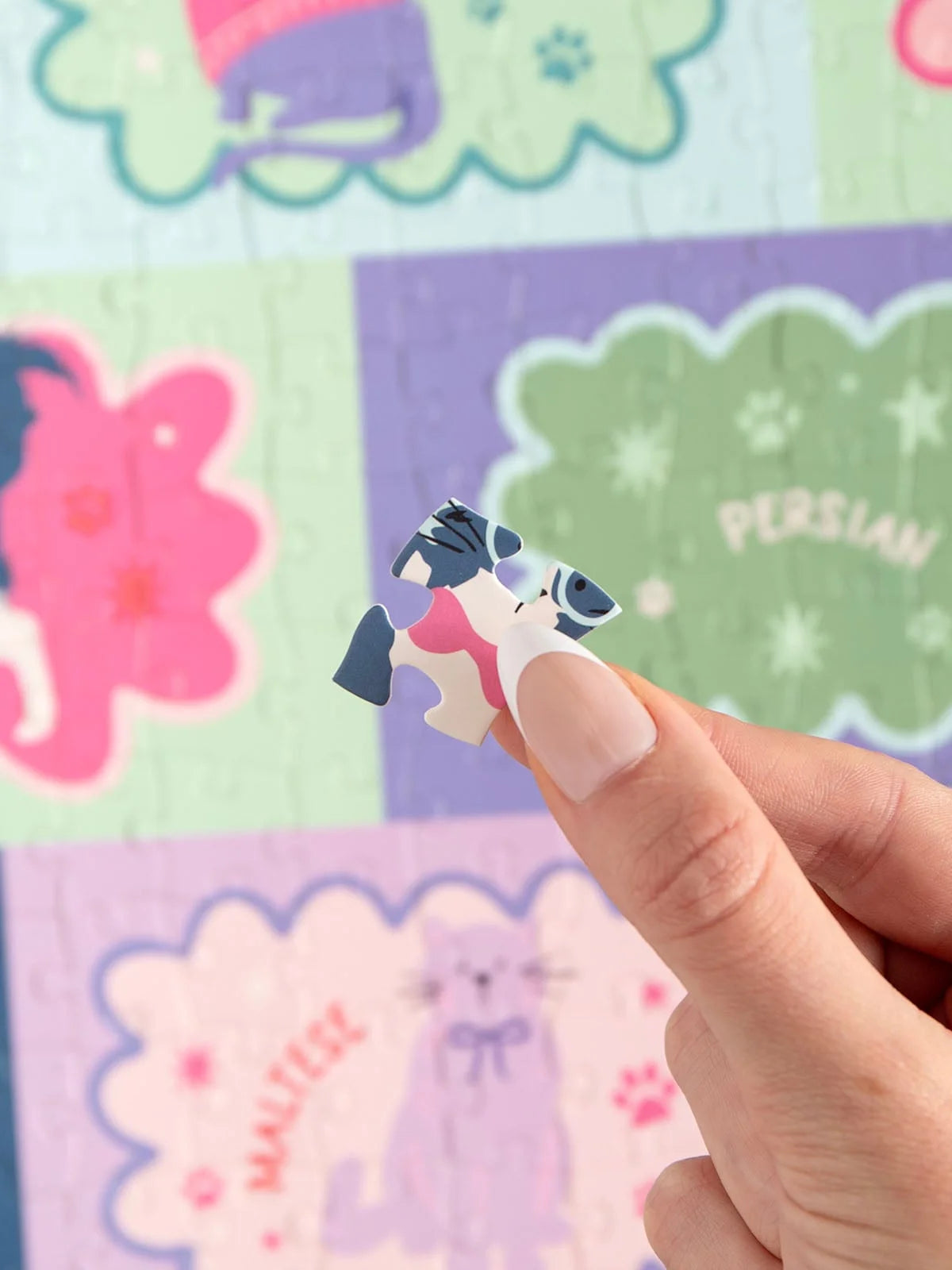 Hand holding a small puzzle piece with a cat design against a colorful background