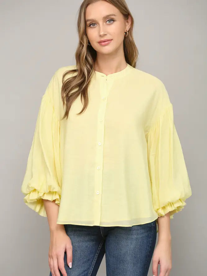 Woman wearing a light yellow blouse with ruffled sleeves on a gray background