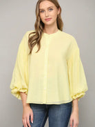Woman wearing a light yellow blouse with ruffled sleeves on a gray background