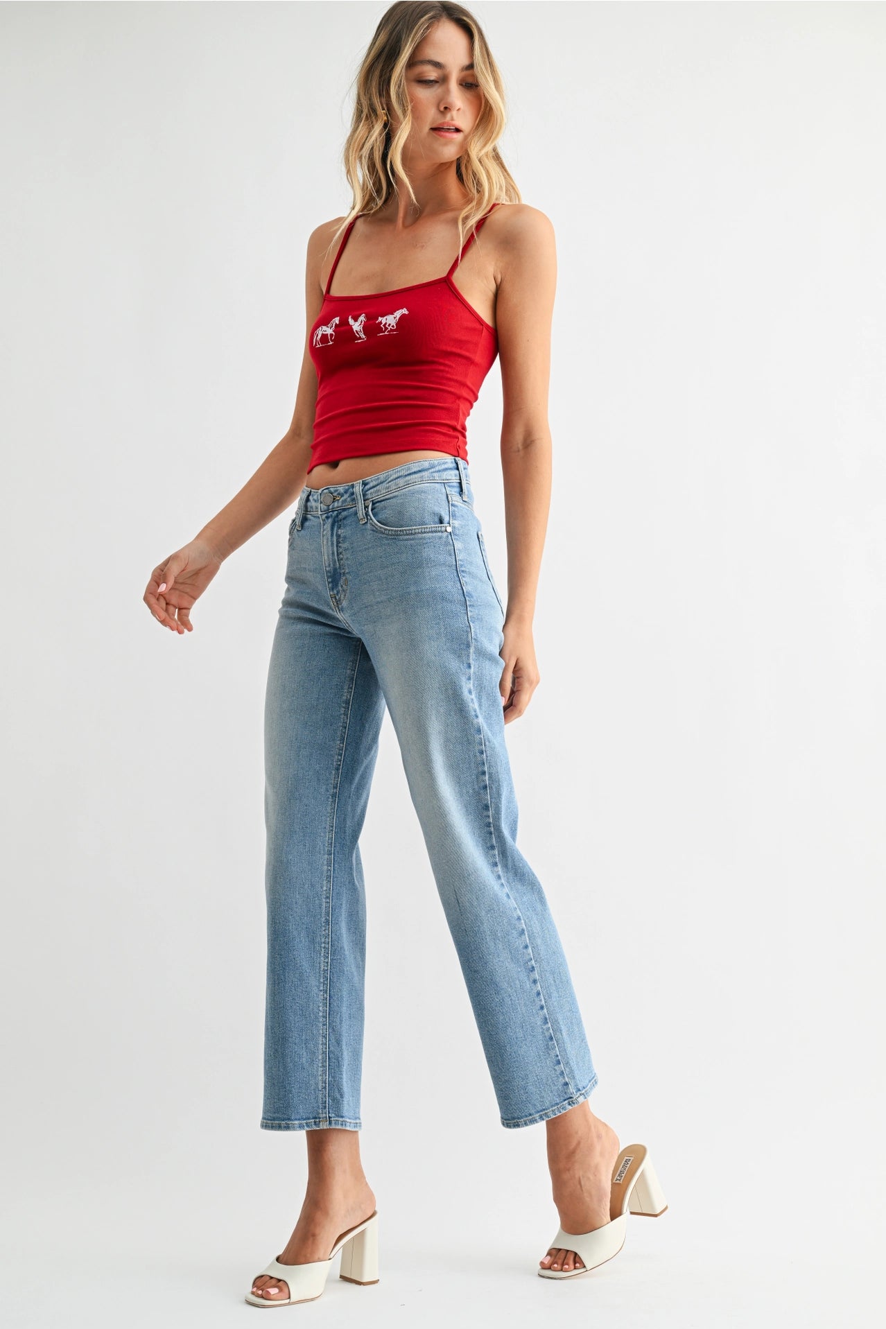 Woman wearing a red tank top and light blue jeans on a white background