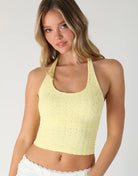 Woman wearing a yellow lace crop top against a plain background