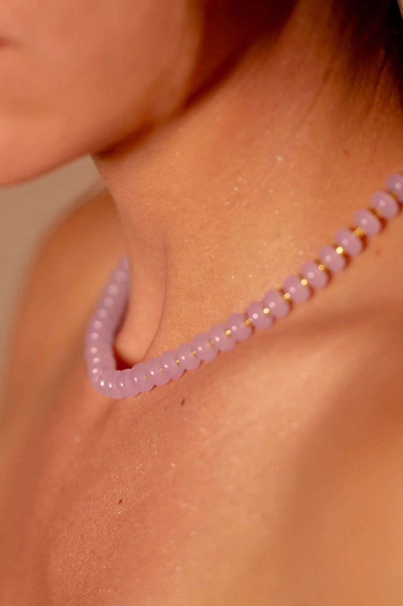Close-up of a person wearing a pink beaded necklace on a neutral background