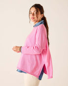 Woman wearing a pink sweater over a denim shirt on a beige background