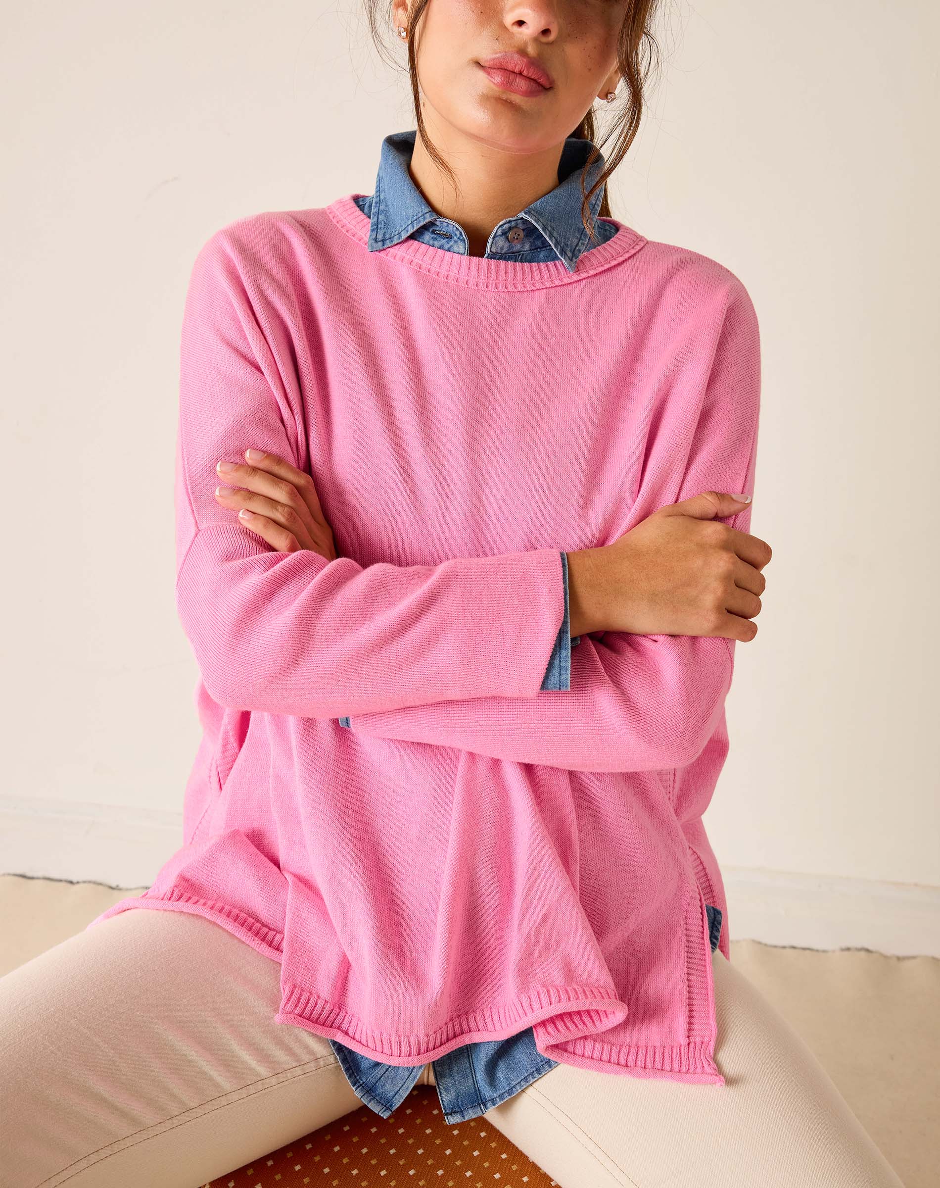 Person wearing a pink sweater with denim collar and cuffs on a neutral background