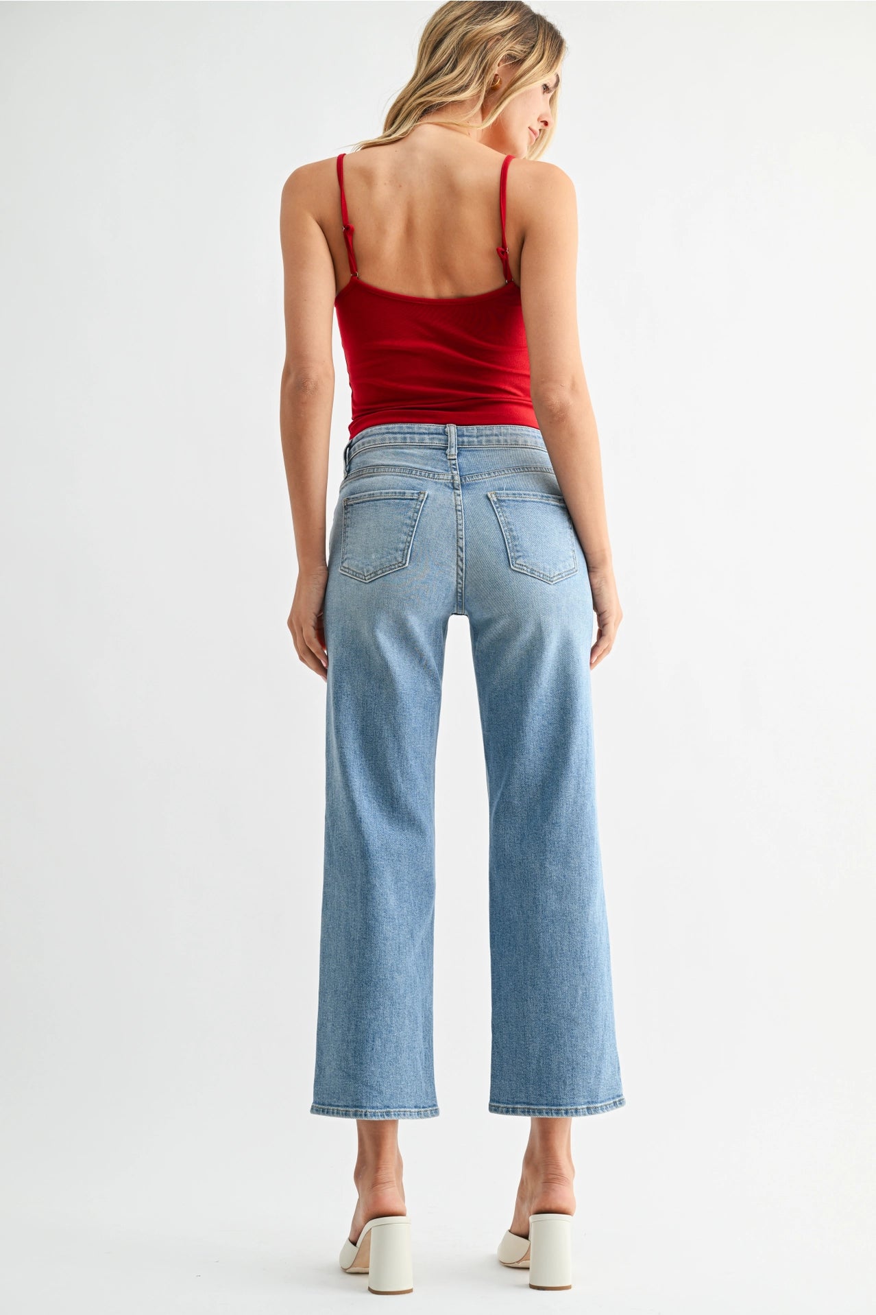 Woman wearing a red tank top and light blue jeans on a white background
