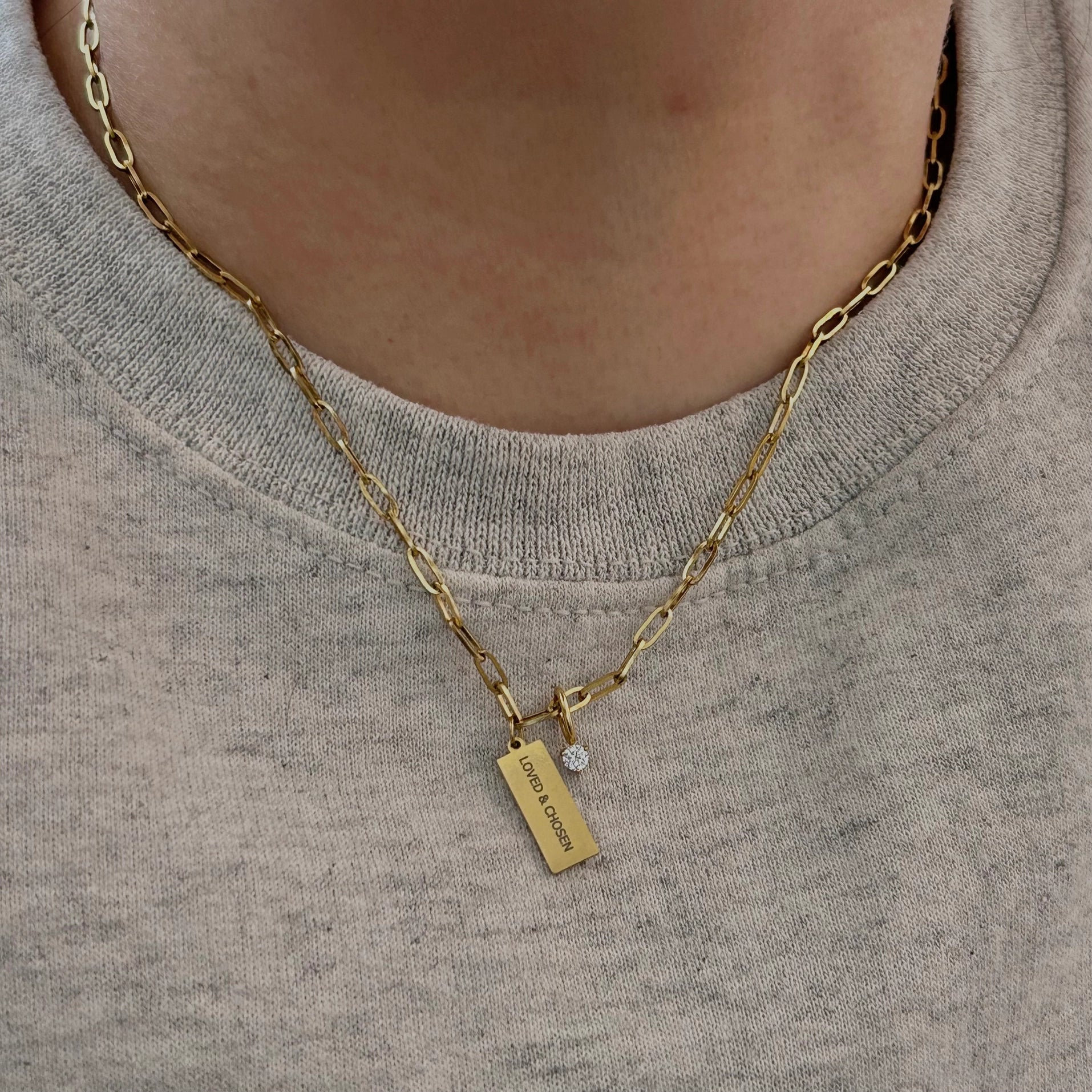 Gold necklace with a pendant on a person wearing a gray shirt