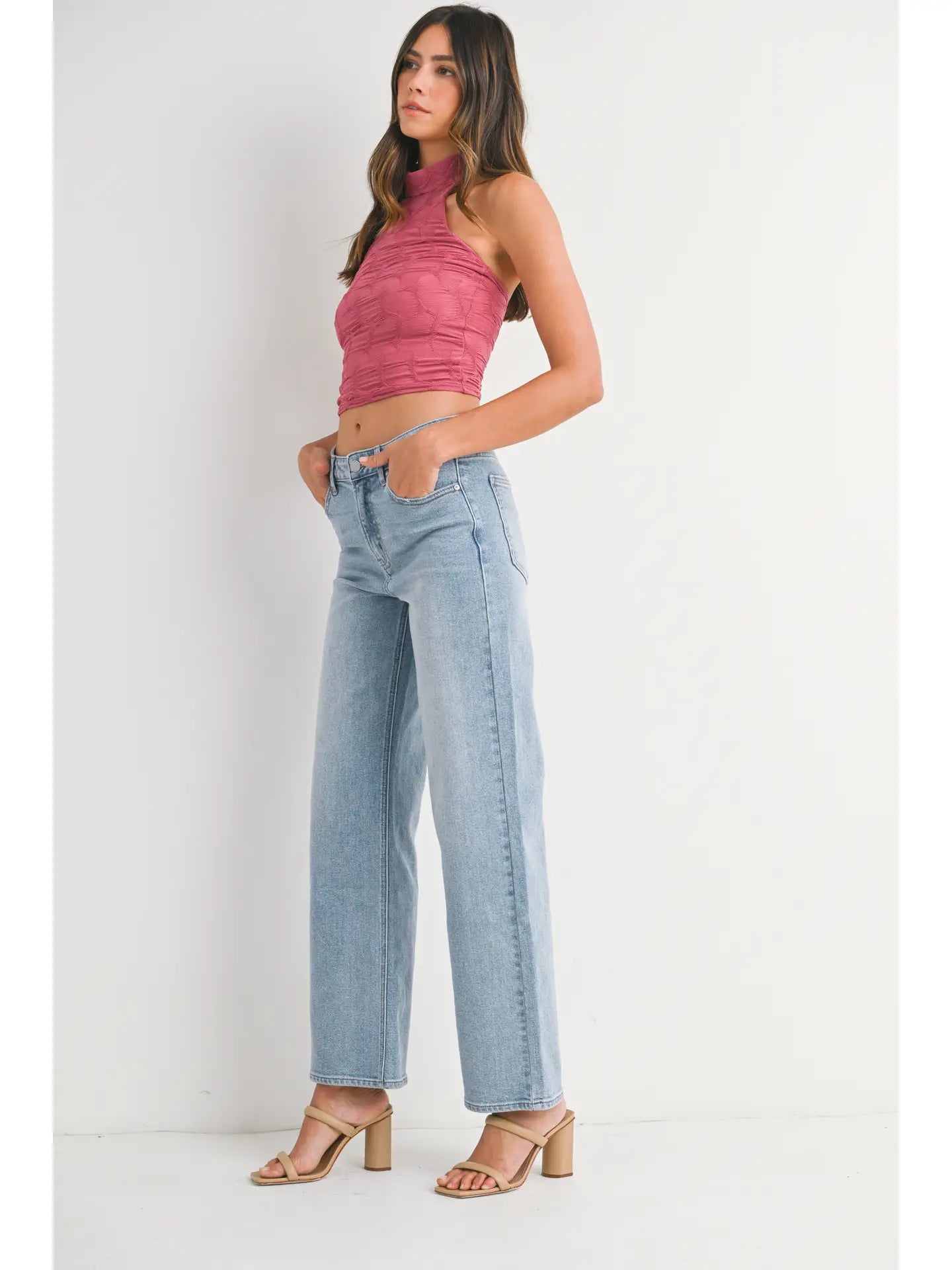 Woman wearing a pink halter top and light blue jeans on a white background