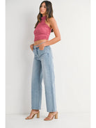 Woman wearing a pink halter top and light blue jeans on a white background