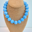 Blue beaded necklace on a brown bust against a light blue background