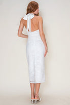 Woman wearing a white lace dress with a halter neck design on a plain background
