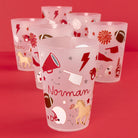 A set of frosted translucent plastic tumblers with red and brown sports-themed illustrations, including football, horses, stars, and the name 'Norman' on the front cup, displayed on a solid red background.