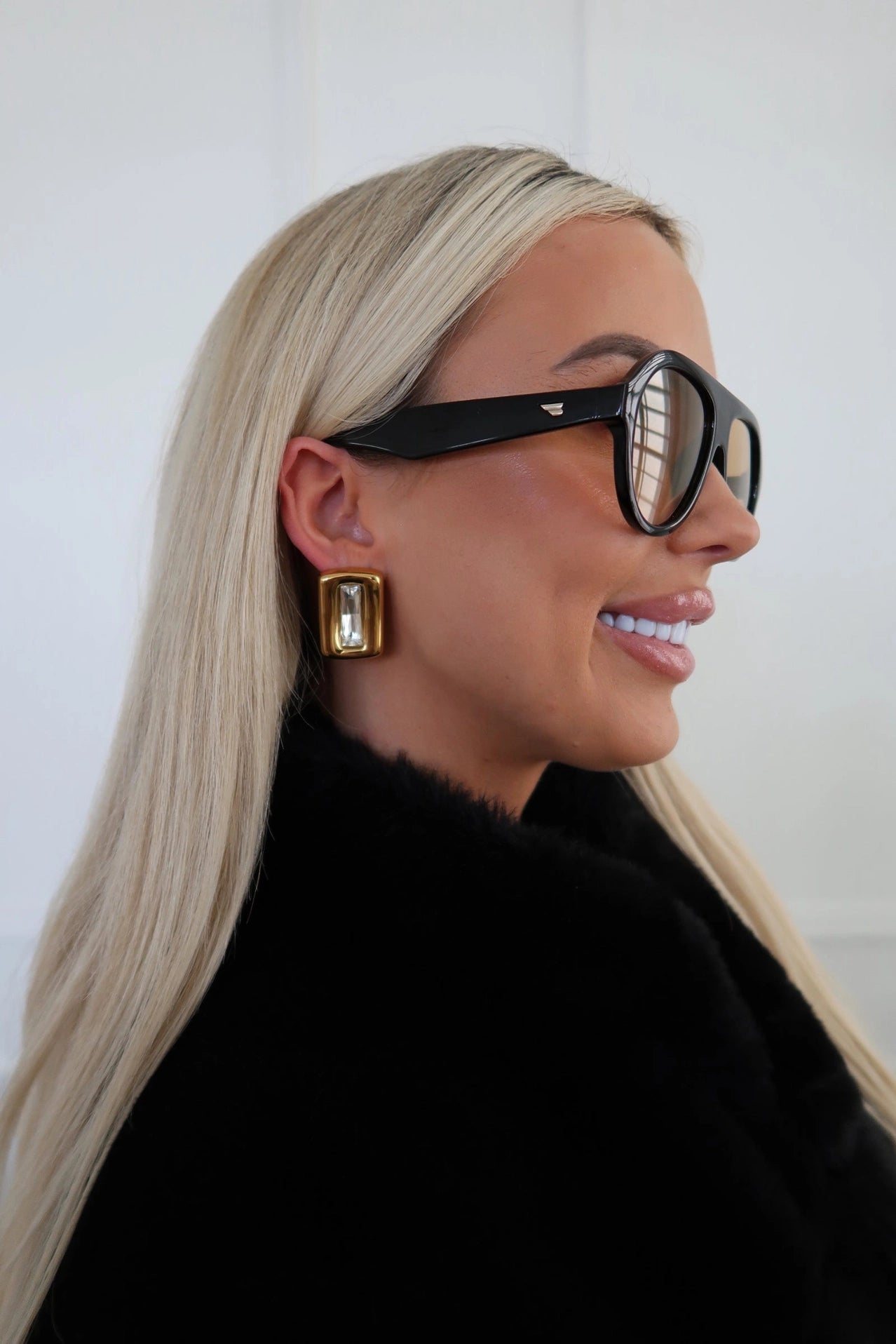 Woman wearing black sunglasses and gold earrings with a plain background