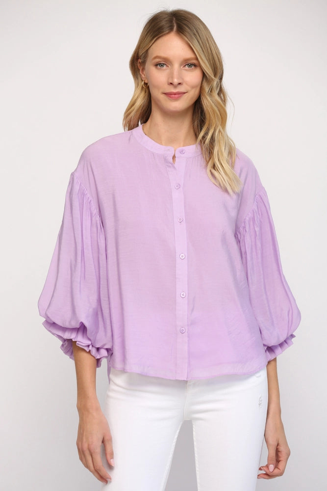 Woman wearing a light purple blouse with white pants on a plain background