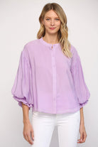Woman wearing a light purple blouse with white pants on a plain background