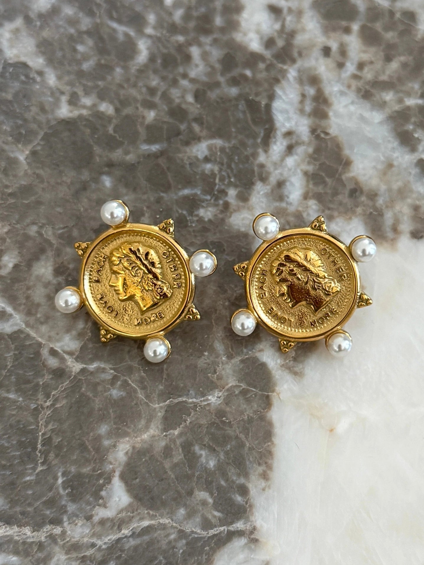 Pair of gold coin earrings with pearls on a marble surface