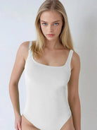 Woman wearing a white bodysuit against a plain background