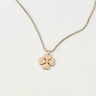 A delicate gold chain necklace featuring a small four-leaf clover pendant with a heart-shaped center, displayed on a clean white background.