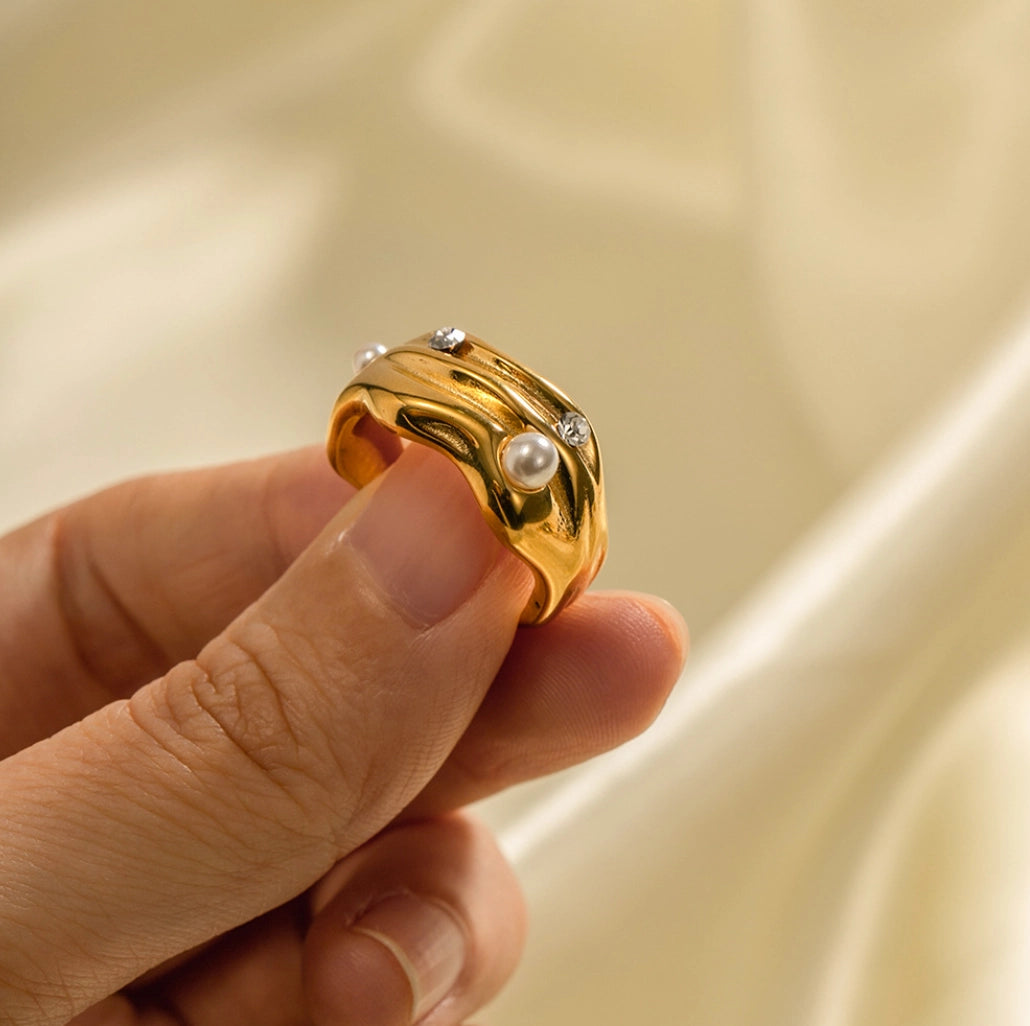 Gold ring with a pearl held by a hand against a beige background