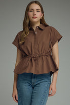 Woman wearing a brown short-sleeve top with a belt and blue jeans on a gray background
