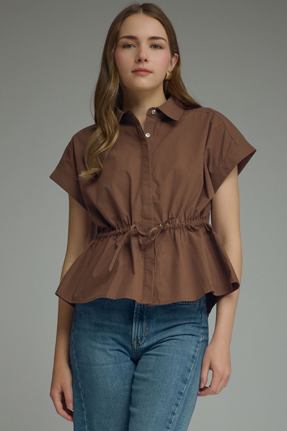 Woman wearing a brown short-sleeve top with a belt and blue jeans on a gray background