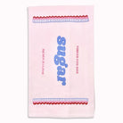 A light pink tea towel featuring a retro sugar-themed design with blue and red embroidered details.